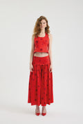 A woman stands against a white background wearing the POLKA FLAME TOP—a sleeveless silk shantung crop top—with a matching long red polka dot embroidered skirt and red high-heeled shoes.