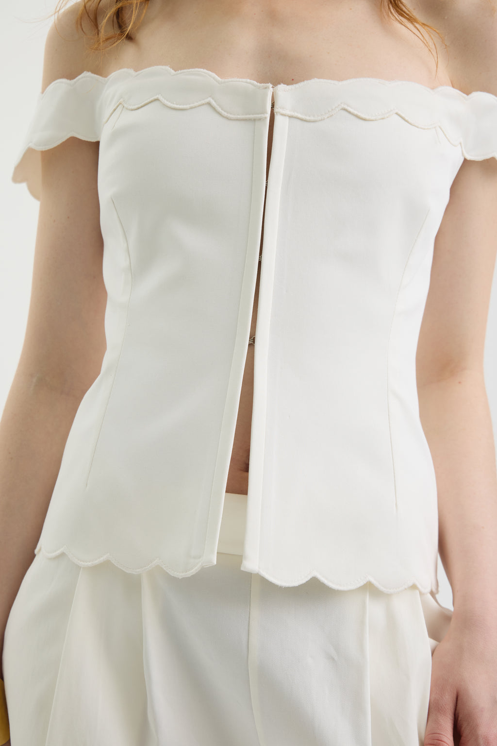 A woman wears the IVORY MUSE TOP with wave-shaped embroidery and scalloped edges, paired with matching white trousers. The photo is cropped at the shoulders and thighs.